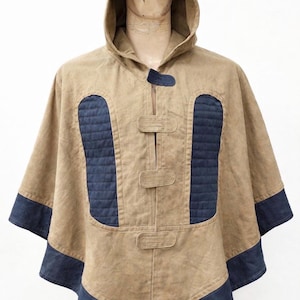 May include: A tan hooded poncho with navy blue detailing. The poncho has a hood, a front closure with three toggles, and navy blue quilted panels on the chest. The sleeves and hem are trimmed with navy blue fabric.