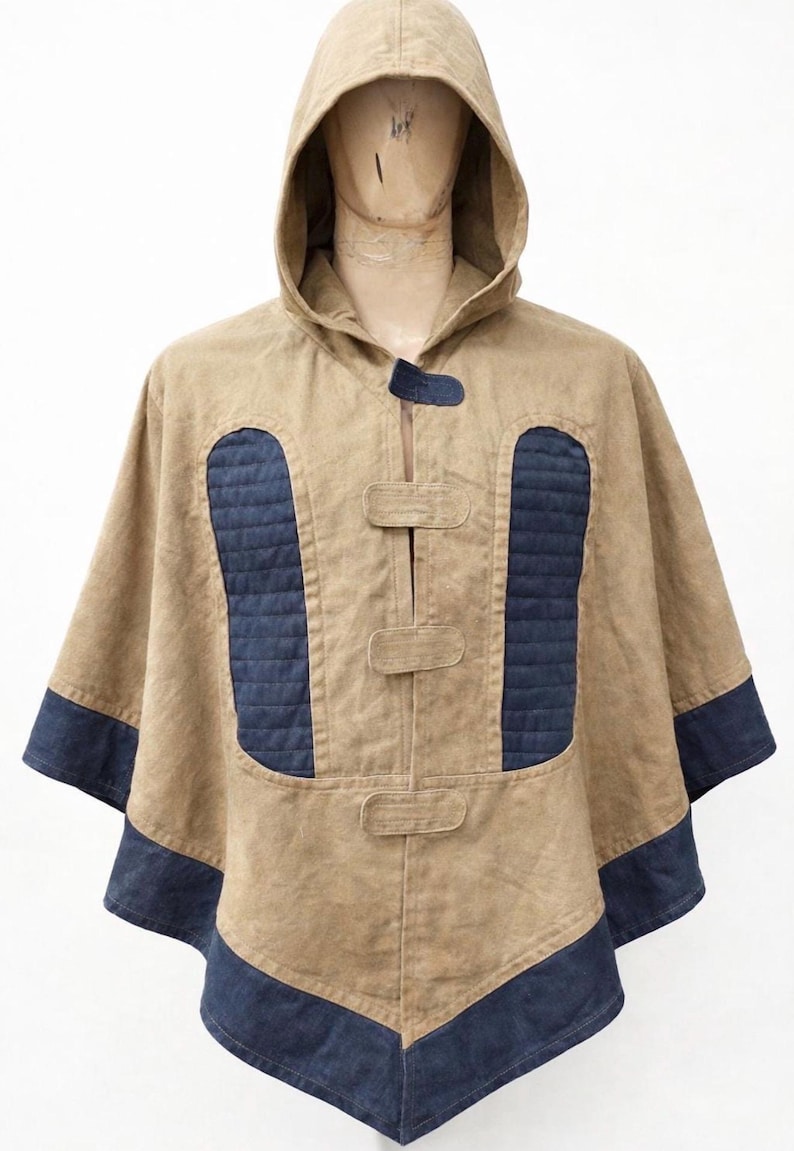 May include: A tan hooded poncho with navy blue detailing. The poncho has a hood, a front closure with three toggles, and navy blue quilted panels on the chest. The sleeves and hem are trimmed with navy blue fabric.