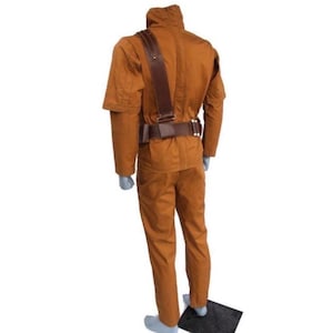 Może przedstawiać: Brązowy kostium składający się z kurtki, spodni i paska. Kurtka ma wysoki kołnierz i pasek na ramię. Pasek ma klamrę i kilka małych kieszeni. Spodnie mają proste nogawki. Kostium jest wykonany z wytrzymałej tkaniny.