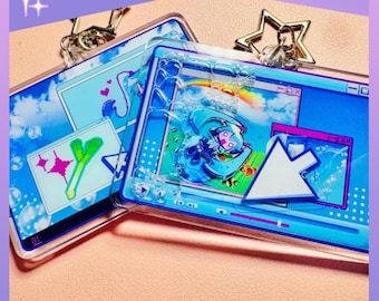 May include: Two rectangular acrylic keychains featuring a blue computer desktop interface design. The keychains include a floating cursor, a character graphic, and a rainbow. One keychain has a star-shaped metal clasp, and the text KARIOAKAS is visible.