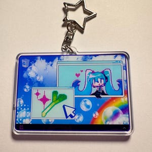 May include: A rectangular acrylic keyring featuring a star-shaped clasp. The design displays a digital desktop interface with a blue sky background, bubbles, a rainbow, and two windows containing pixel art of a teal-haired character and a leek.