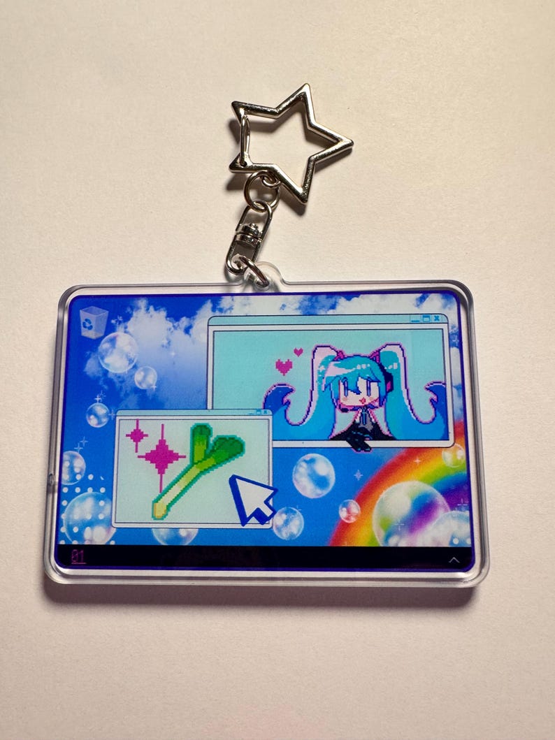 May include: A rectangular acrylic keyring featuring a star-shaped clasp. The design displays a digital desktop interface with a blue sky background, bubbles, a rainbow, and two windows containing pixel art of a teal-haired character and a leek.