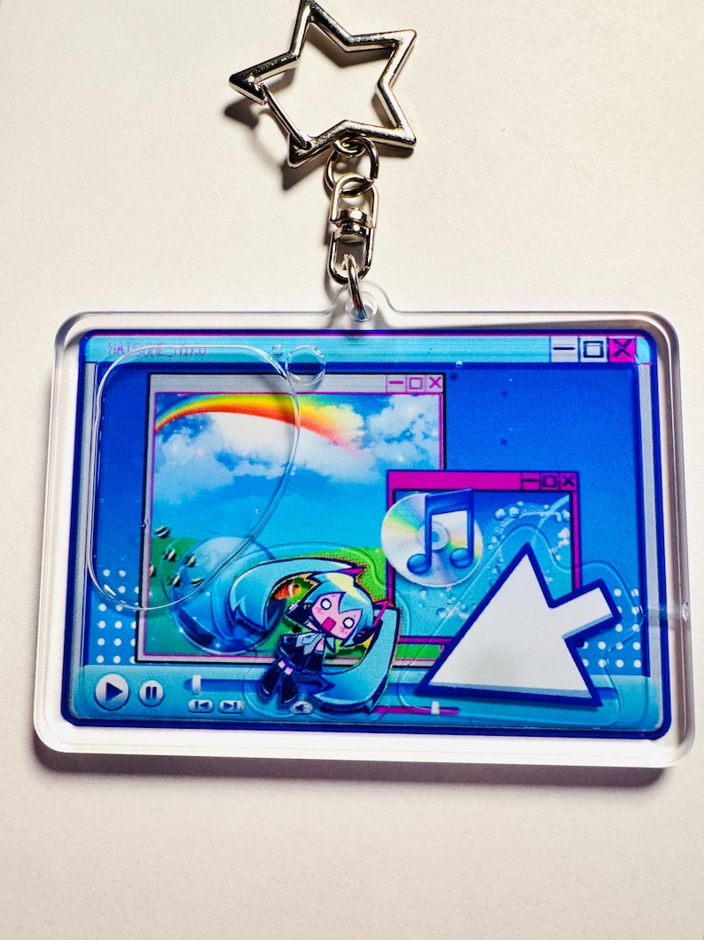 May include: A rectangular acrylic keyring featuring a star-shaped metal clasp. The design displays a retro computer interface with a blue background, a rainbow, a music note icon, and a stylised anime character with teal hair and a large cursor.