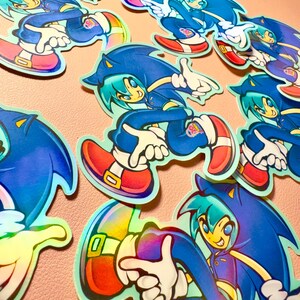 May include: Multiple die-cut stickers featuring a stylized anime-inspired character wearing a blue hooded jacket with spiky hair, white gloves, and red shoes with gold buckles. Each sticker displays a small circular logo with the text 20th Anniversary.