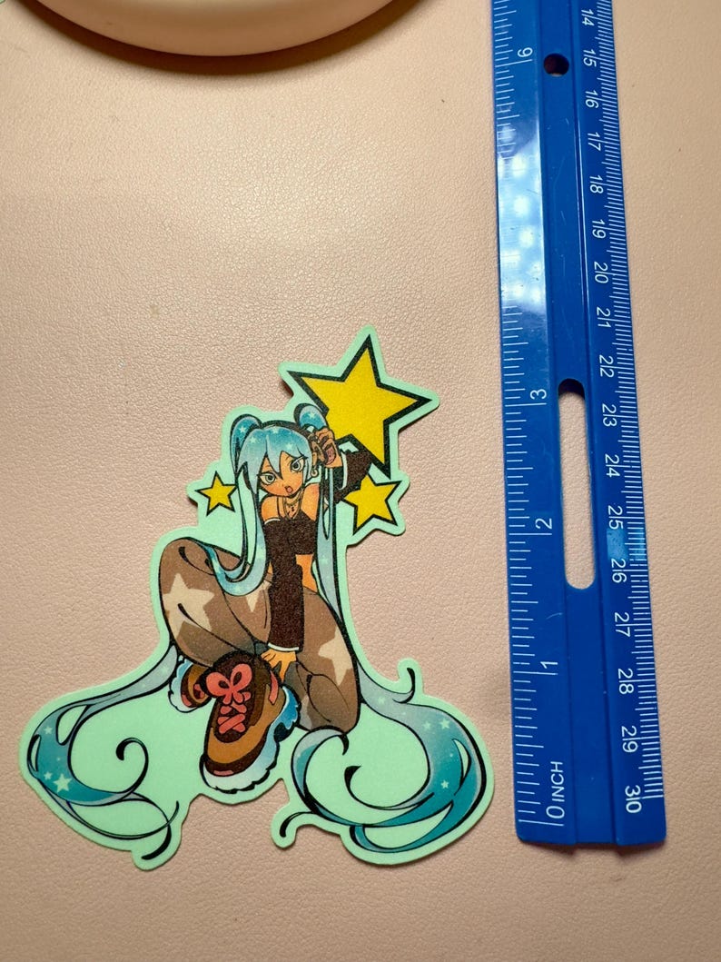 May include: A die-cut sticker featuring an anime-style character with long light blue hair, wearing a brown top and pants, posed with three yellow stars. A blue ruler is placed next to the sticker, showing it measures approximately 3.5 inches tall.