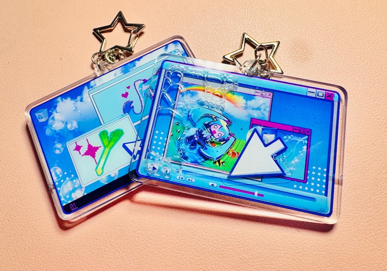 May include: Two rectangular acrylic keychains with star-shaped clasps, featuring a digital interface design with blue windows, a white mouse cursor, a cartoon character, a rainbow, and a green leek graphic, with clear bubbles inside the acrylic.