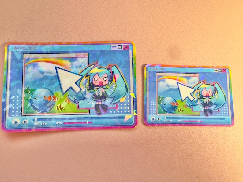 May include: Two holographic stickers featuring a cartoon character with blue hair and a blue and white background. The stickers are shaped like computer windows with a cursor and the text "HATSU-NE-MIKO"