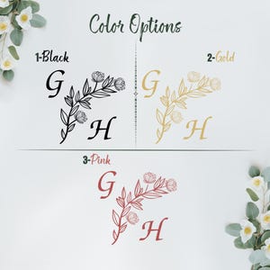 Op de afbeelding: Drie kleuropties voor een bloemig monogramontwerp. Het ontwerp bevat de letters "G" en "H" met een bloemtak en bladeren. De kleuropties zijn zwart, goud en roze.