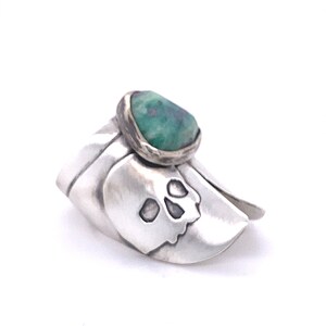 Könnte beinhalten: Ein silberner Ring mit einem Totenkopfdesign und einem grünen Edelstein, der oben eingesetzt ist.