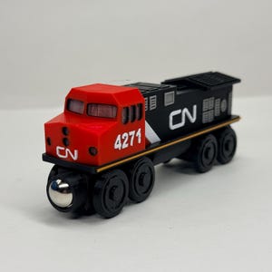 May include: A toy train engine featuring a red cab and a black body with the white text CN and the number 4271 printed on the side. The locomotive has black wheels with metallic silver centres and a detailed exterior design with vents and windows.