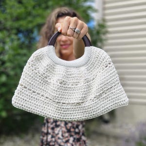 May include: A white crocheted bag with a wooden handle. The bag has a scalloped edge and a delicate openwork design.