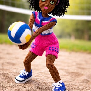 Puede incluir: Muñeca de ganchillo hecha a mano de una jugadora de voleibol. La muñeca viste un conjunto rosa y azul, zapatillas blancas y azules y una diadema con un pompón. La muñeca sostiene un balón de voleibol con paneles azules, blancos y amarillos.