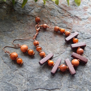 May include: A set of wooden bead earrings and a bracelet with copper accents. The earrings and bracelet feature brown and orange wooden beads and dark brown wooden rectangular beads.