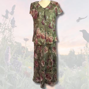 Puede incluir: Un conjunto floral de dos piezas con una blusa de manga corta y una falda larga. El conjunto presenta una base verde con un estampado de flores rosas y burdeos. La blusa tiene un escote en V y cierre de botón. La falda es larga.