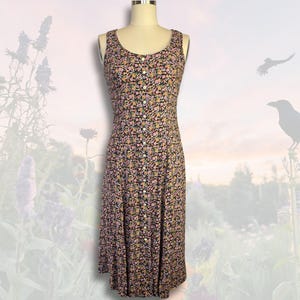 May include: A sleeveless, button-down dress with a floral pattern in pink, yellow, and green on a black background. The dress is displayed on a mannequin. The dress has a scoop neckline and a fitted bodice that flows into a flared skirt.