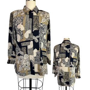 May include: A long-sleeved button-down shirt featuring a patchwork design in navy blue, tan, and cream. The pattern consists of various intricate paisley and ornate floral motifs arranged in rectangular blocks across the front and back panels.