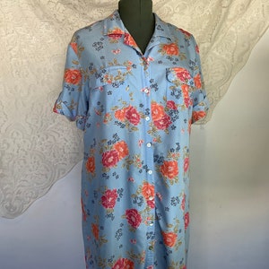 May include: A light blue button-down shirt dress with a floral print featuring pink, red, and orange flowers. The dress has short sleeves and a collared neckline.