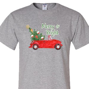 May include: A gray t-shirt with a red vintage car carrying a Christmas tree with ornaments. The text "Merry & Bright" is printed on the shirt.