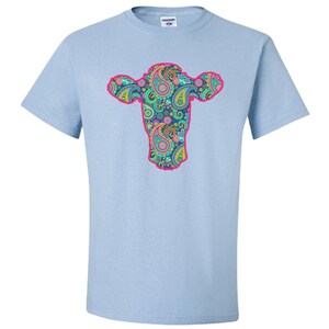May include: Light blue t-shirt featuring a pink outline of a cow's head filled with a paisley pattern in shades of blue, green, pink, and yellow.