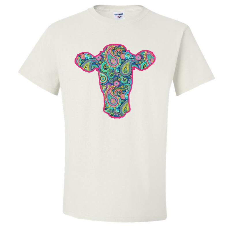 May include: White t-shirt featuring a pink outline of a cow's head filled with a paisley pattern in shades of blue, green, pink, and yellow.