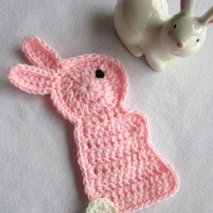 May include: A pink crocheted bunny with a white button on its foot. The bunny has a black eye and is made with a soft yarn.
