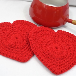 May include: Two red crocheted heart-shaped pot holders. The pot holders are made with a thick yarn and have a raised texture.
