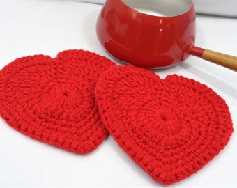 May include: Two red crocheted heart-shaped pot holders. The pot holders are made with a thick yarn and have a raised texture.