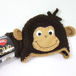 May include: Brown crocheted monkey hat with a brown felt face and large white eyes. The hat has a brown crocheted brim and ear flaps.