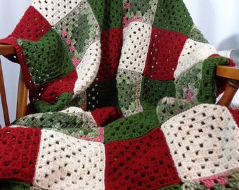 May include: A crocheted blanket with squares in red, green, and cream colors. The blanket is draped over a wooden chair.