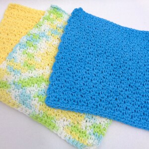 May include: Three crocheted dishcloths in yellow, green, white, and blue. The dishcloths are made with a simple crochet stitch.