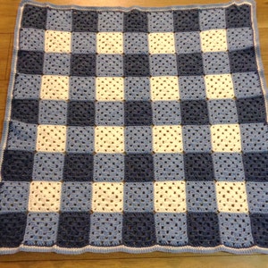May include: A handmade crochet blanket featuring a checkerboard pattern. The squares alternate between white, light blue, and navy blue. The blanket has a light blue border.