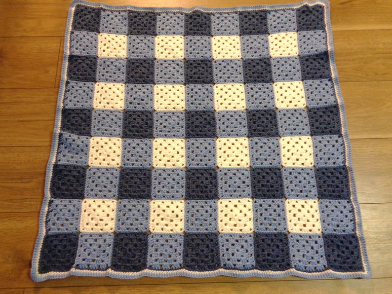May include: A handmade crochet blanket featuring a checkerboard pattern. The squares alternate between white, light blue, and navy blue. The blanket has a light blue border.