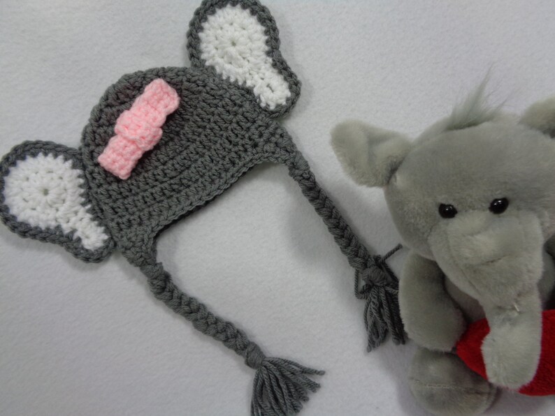 May include: Gray crocheted elephant hat with pink bow and white ears. The hat has a long gray braid that can be tied under the chin.