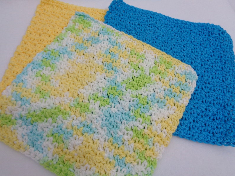 May include: Three crocheted dishcloths in yellow, blue, and a multi-colored pattern of yellow, green, white, and blue.