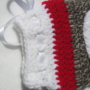 May include: White crocheted boot cuff with red and brown stripes and a white satin ribbon tied around the top.