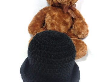 May include: A black fuzzy bucket hat with a brown teddy bear sitting behind it.
