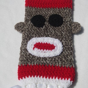 May include: Crocheted sock monkey doll with red and white stripes, brown fur, black eyes, and a red mouth. The doll has white ribbon ties.