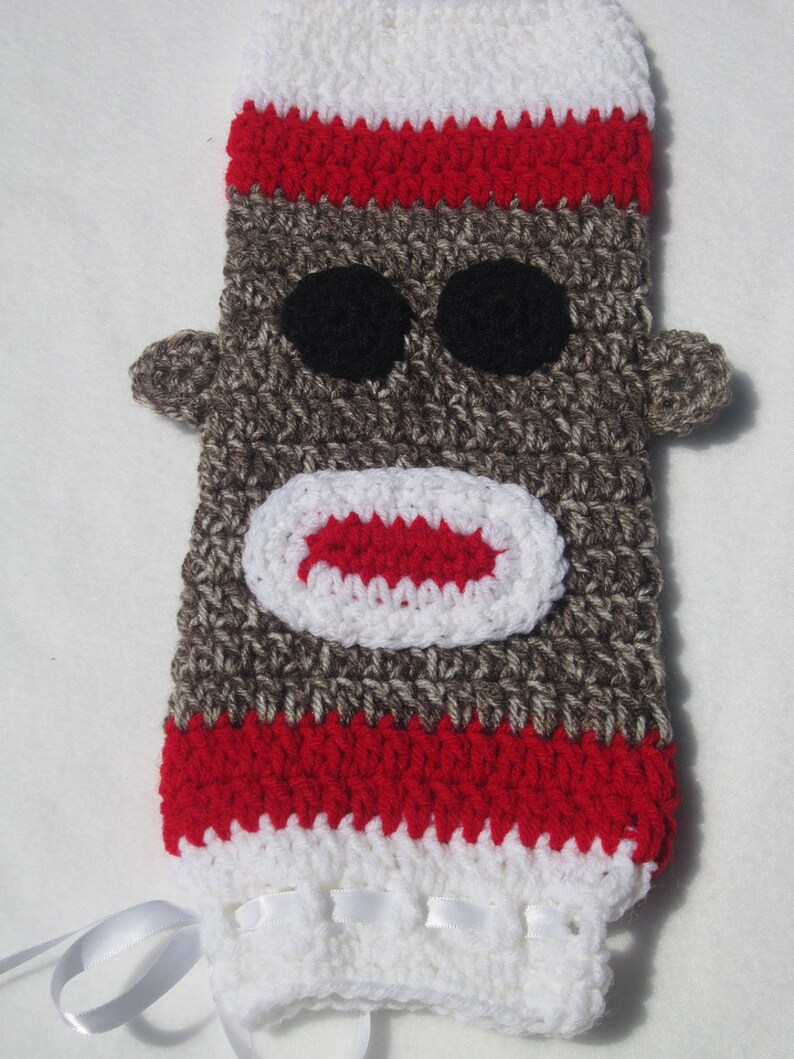 May include: Crocheted sock monkey doll with red and white stripes, brown fur, black eyes, and a red mouth. The doll has white ribbon ties.