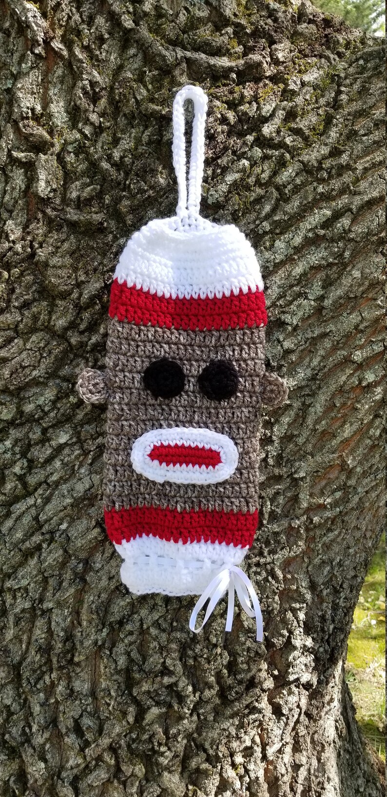 May include: Crocheted monkey sock puppet with a white loop handle. The monkey has a brown face with black eyes, a red mouth, and red and white stripes around the head.
