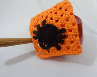 May include: Orange crocheted coaster with a black spider applique. The coaster is square-shaped and has a textured, open weave design. The spider is centered on the coaster, adding a Halloween theme.