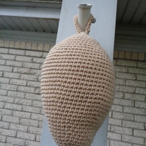 May include: A beige crocheted bottle cozy with a white crocheted loop at the top.