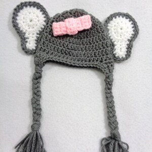 May include: Gray crocheted hat with white crocheted ears and a pink bow. The hat has long gray braided tails with tassels.