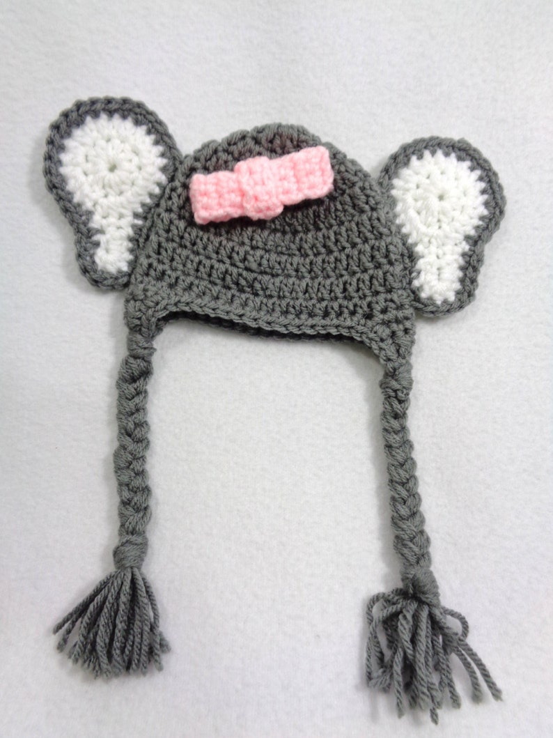 May include: Gray crocheted hat with white crocheted ears and a pink bow. The hat has long gray braided tails with tassels.
