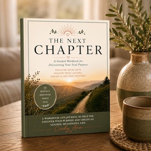 May include: A hardcover book titled The Next Chapter, A Guided Workbook for Discovering Your Soul Purpose by Cindy Ann. The cover features a sunset landscape with a path, a sunburst icon, and text detailing the workbook and journal contents.