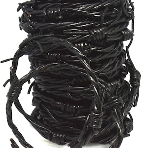 May include: A tightly coiled roll of black barbed wire. The wire is thick and has a dark, glossy coating. The barbs are evenly spaced along the wire, creating a sharp, industrial appearance. The image is set against a white background.
