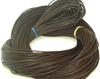 May include: Dark brown leather cord coiled in a circular shape. Two bundles of the cord are secured with blue and yellow rubber bands. The cord appears to be smooth and uniform in thickness, suitable for crafting or jewelry making.