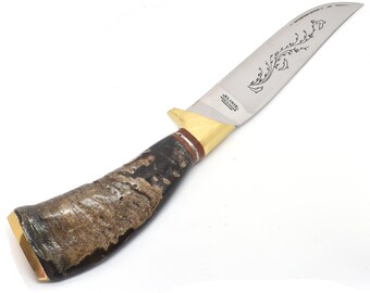Puede incluir: Cuchillo de caza con una hoja de acero pulido con un diseño floral grabado. El mango es de material oscuro y texturizado con detalles dorados y marrones. El cuchillo tiene una hoja curva y una apariencia robusta.
