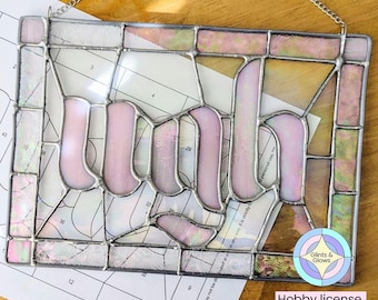 May include: A stained glass window panel with the word "Ruth" in a pink iridescent glass. The panel is framed in silver and has a grid pattern behind it. The panel is labeled "Hobby license pattern" and "Glints & Glows".