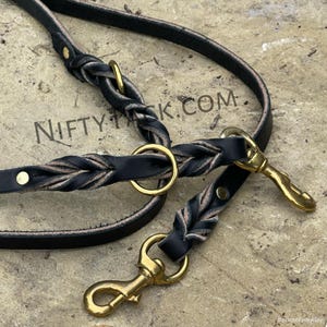 May include: Two black leather dog leashes with brass hardware. One leash is braided and the other is flat. Both leashes have a brass ring and a brass snap hook.