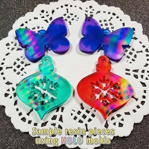 May include: Four resin pieces, two butterfly and two ornament shapes, with a holographic finish. The butterflies are blue and purple, the ornaments are green and red. The ornaments have a snowflake design.